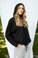 Model wearing Annie Light Ponte Hoodie in Black with drawstring hem and cross-front hood.